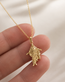 Gold necklace with a leaf-shaped pendant held by a hand against a neutral background